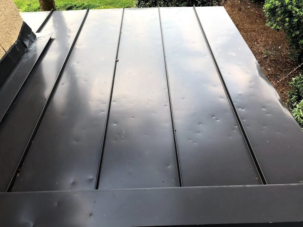 Hail-dented standing seam panel and vent on a Comfort ranch home